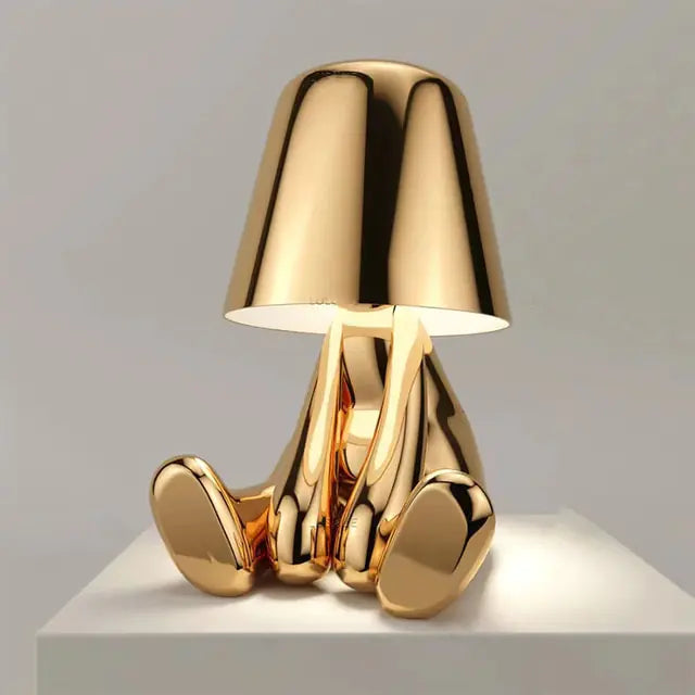 Gold table lamp with a small man figure silhouette, emitting a soft and gentle light.